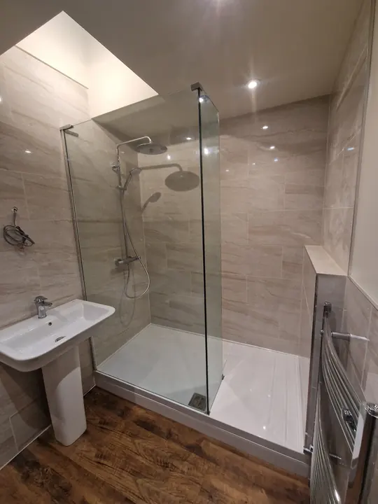 A finished shower room with a walk-in shower, glass screen, pedestal basin and chrome towel rail under a roof light.