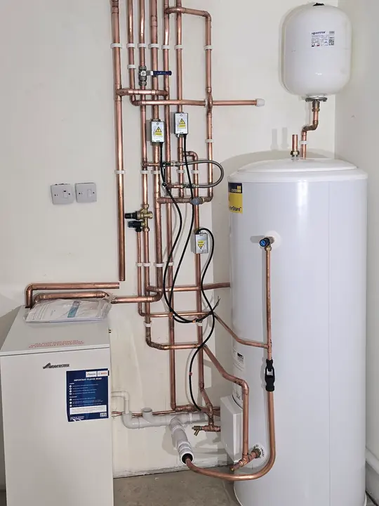 A floor-standing boiler and unvented hot water cylinder connected with clipped copper pipework.