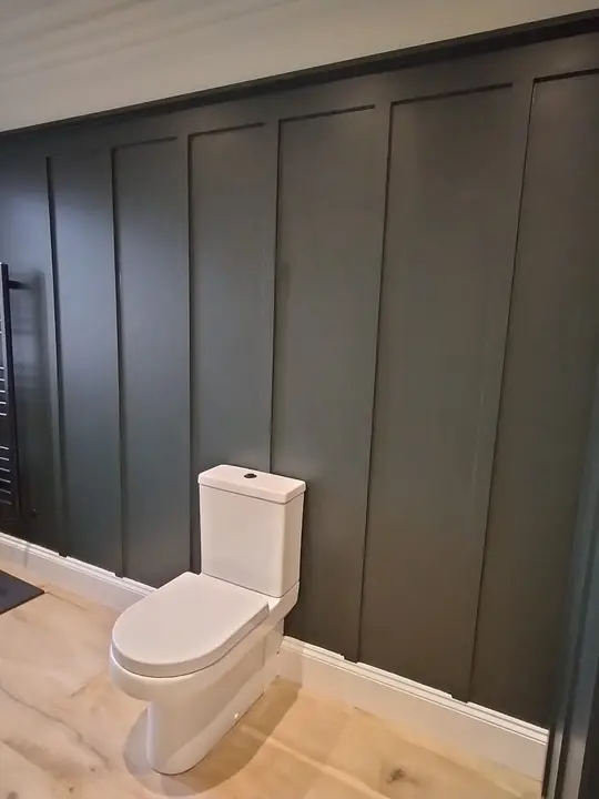 A bathroom with dark green panelled walls, a close-coupled toilet, a black towel radiator and an oak floor.
