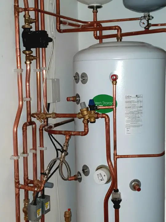 Copper pipework, valves and two expansion vessels fitted around an unvented hot water cylinder in a cupboard.