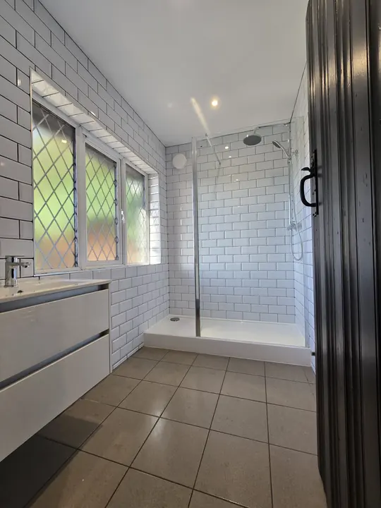 A shower room with white metro tiles, a walk-in shower, a white vanity unit and leaded windows.