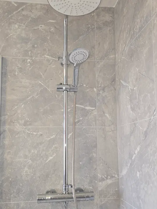 A chrome thermostatic shower with a large overhead rain head against grey marble-effect wall panels.