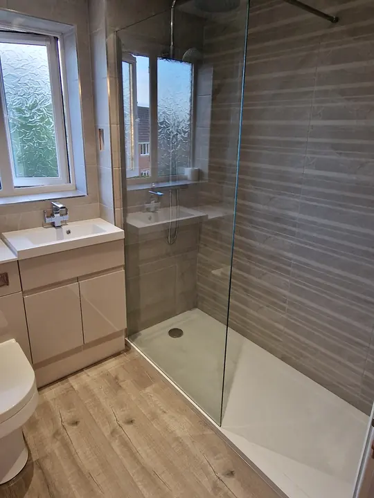 A shower room with a walk-in shower and glass screen, a vanity basin, a toilet and a wood-effect floor.