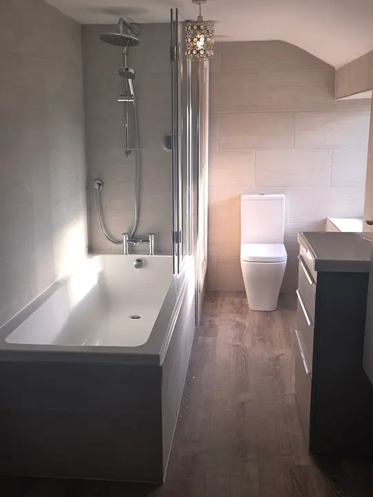 A bathroom with a bath and shower screen, a thermostatic shower, a close-coupled toilet and a dark wood-effect floor.