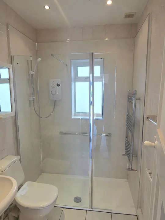 A walk-in shower with an electric shower, a grab rail and a glass screen, beside a toilet and basin.