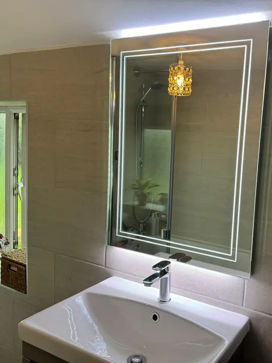 A basin and chrome mixer tap beneath a backlit LED mirror in a tiled bathroom.