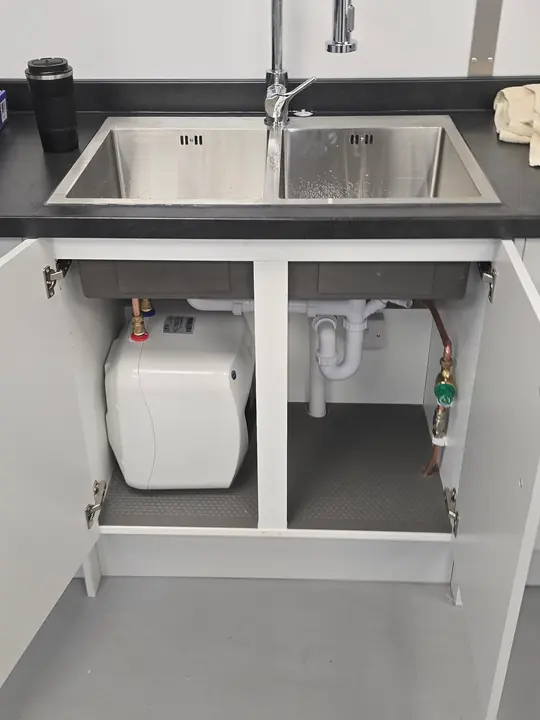 A stainless steel kitchen sink with a pull-down tap and a small water heater fitted in the cupboard below.