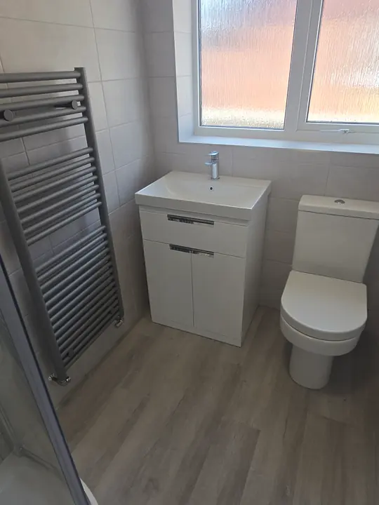A bathroom with a vanity basin, a close-coupled toilet and a grey towel radiator under a frosted window.