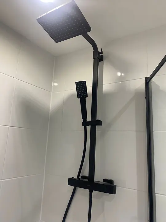 A matt black thermostatic shower with a square rain head and handset on white tiled walls.